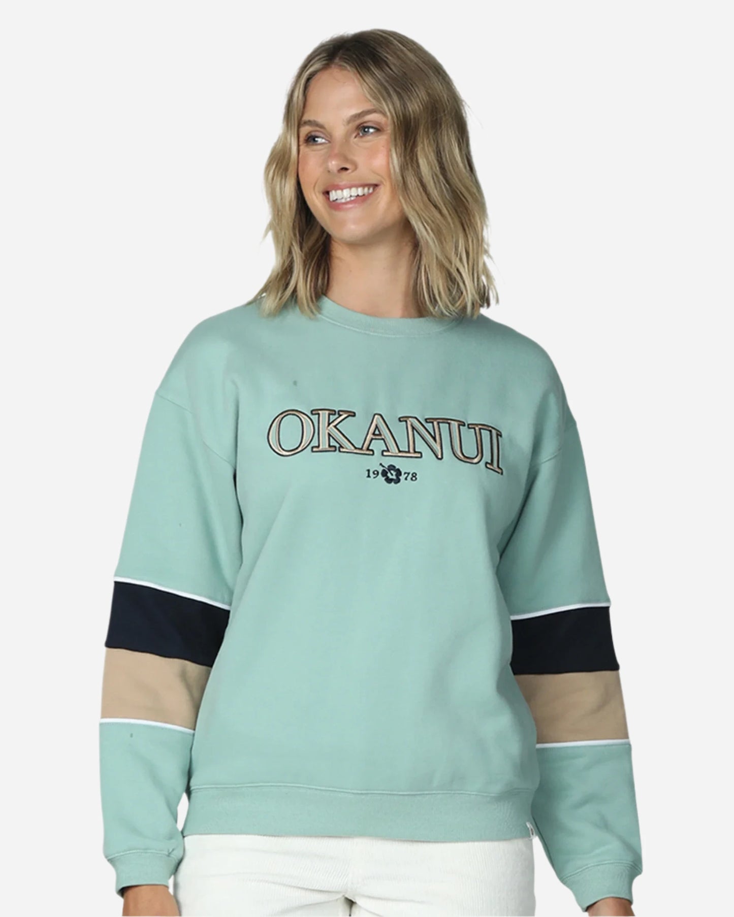 A womens winter sweater in color sage showing the embroided logo of Okanui. 