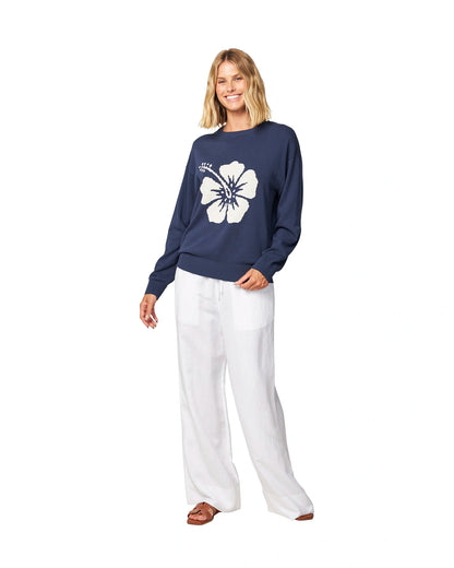 Full body front view of a female model wearing the Okanui waffle knit jumper in navy color paired with white trousers