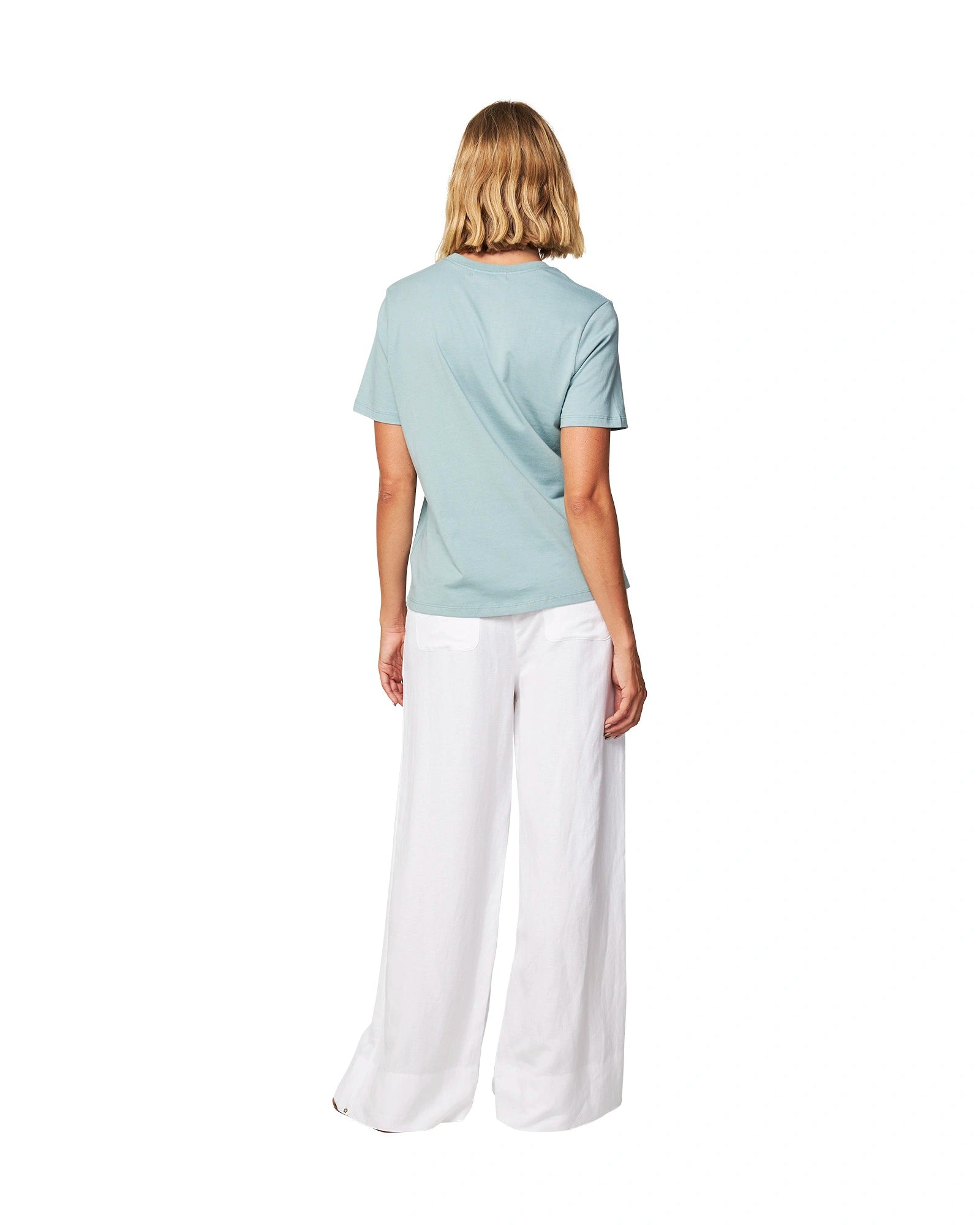 Full body of a female model wearing a t-shirt paired with the Okanui wide leg linen beach pants in white color