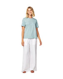 Full body front view of a female model wearing a blue shirt paired with the Okanui wide leg linen beach pants in white color