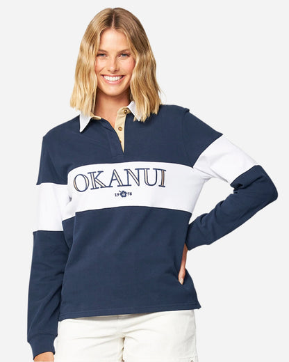 A female model with one hand in her hip pose wearing the Okanui Heritage rugby top jumper in Navy/White color