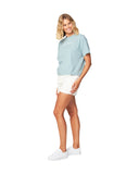 One leg in front pose of a female model wearing the Okanui Tour Cropped cotton T-shirt in Sage variant