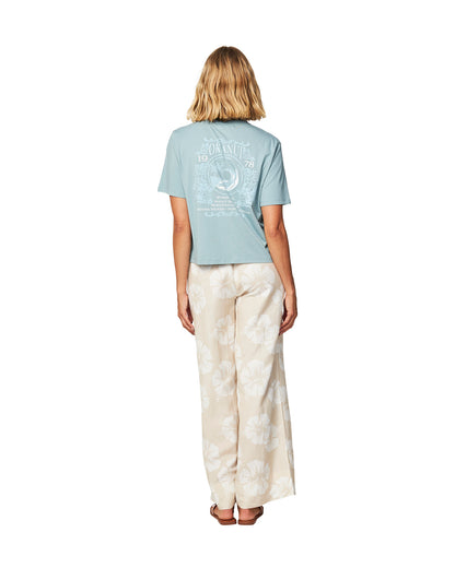 Full body back view of a female model wearing the Okanui Tour Cropped cotton T-shirt in Sage variant paired with Okanui hibiscus print trouser