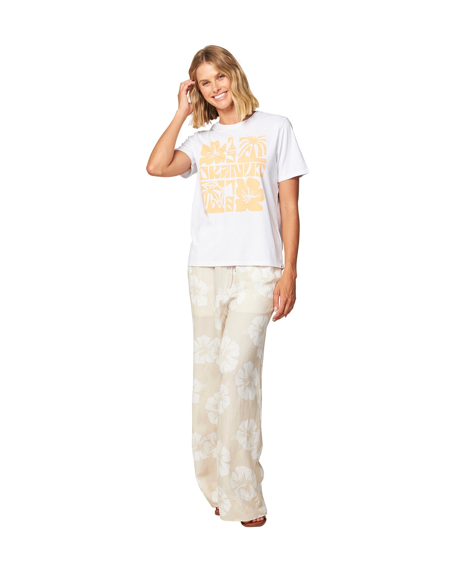 Full body front view of a female model wearing the Okanui Waterways cotton T-shirt in White color paired with white Hibiscus print trouser