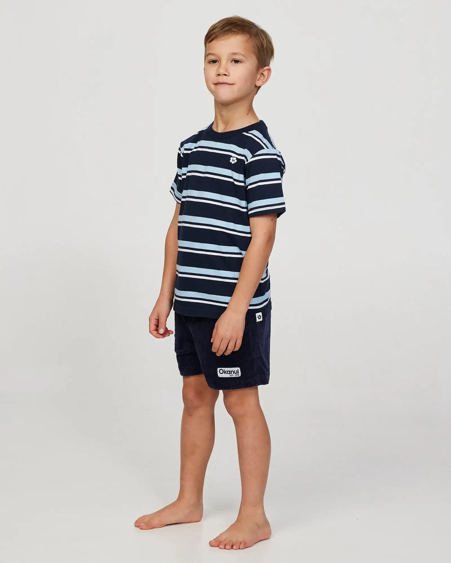 Front-left view of a little boy model wearing the Okanui Corduroy Walk Short in Iron Navy