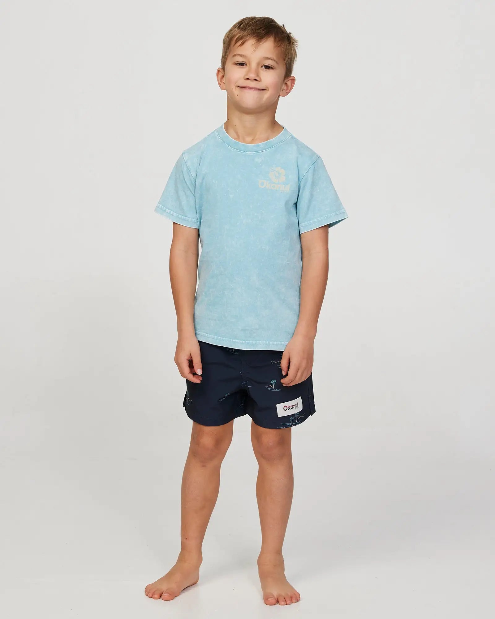 Full body front view of a little boy model wearing the Okanui Isle stretch swim short for boys in Black