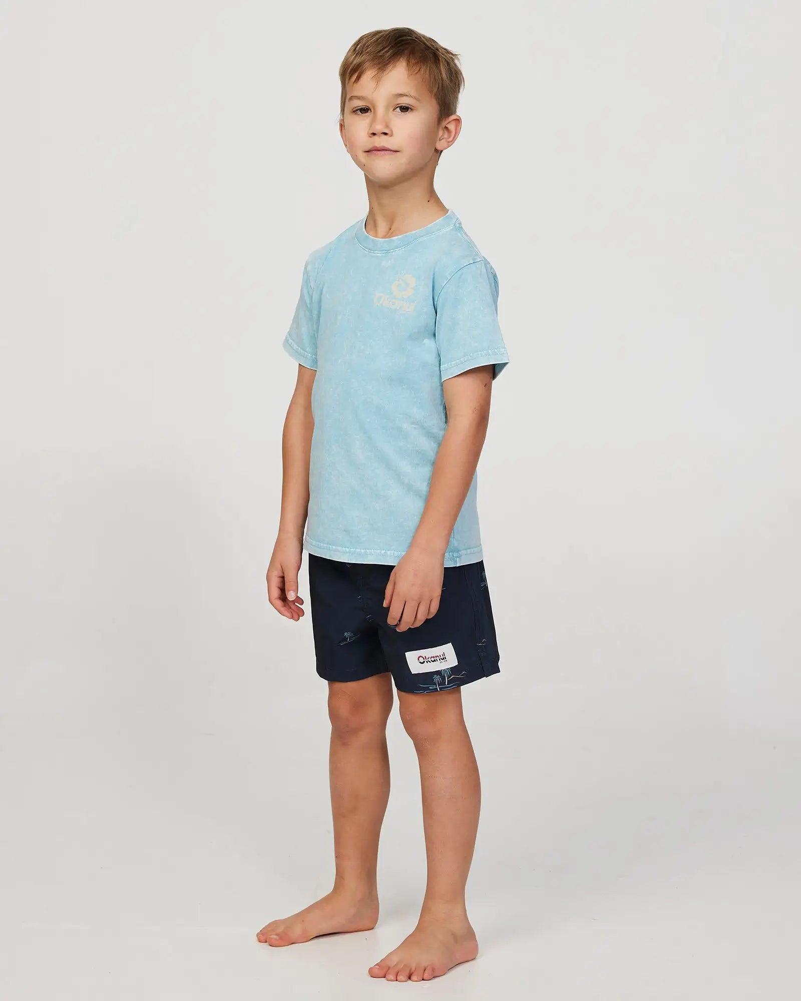 Full body front-left view of a boy model wearing the Okanui Isle stretch swim short for boys in Black