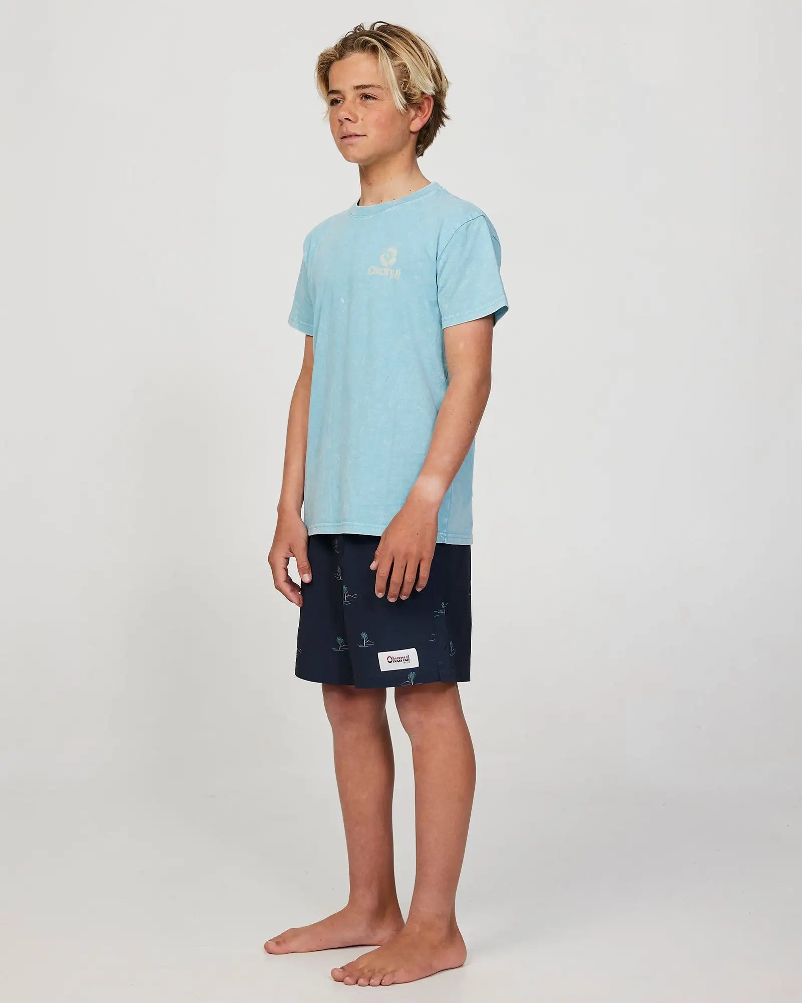 Full body front-left view of a boy model wearing the Okanui Isle stretch swim short for boys in Black