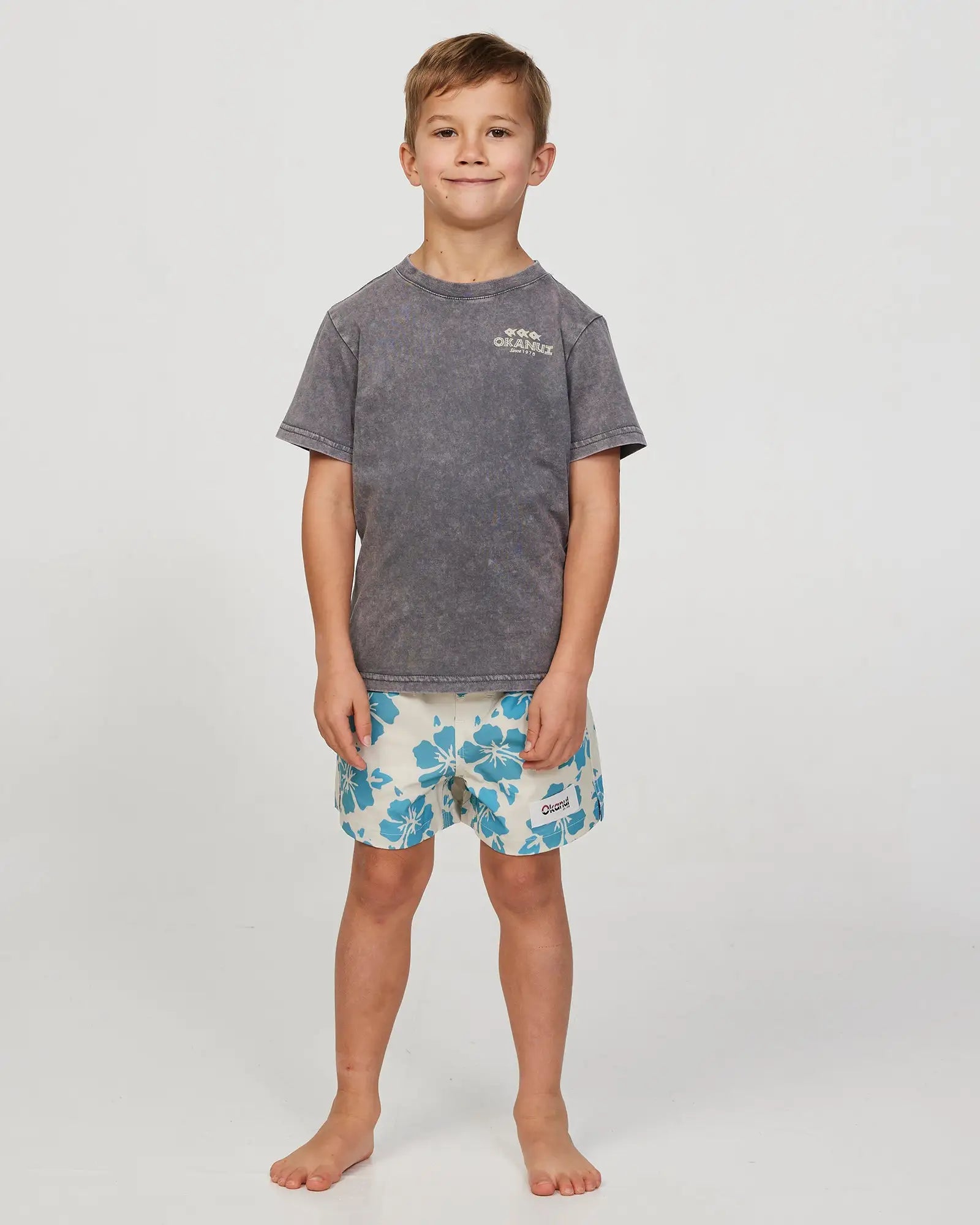 Full body front view of a little boy model wearing the Okanui Waterworld Stretch Swim Short for Boys in Stone Aqua