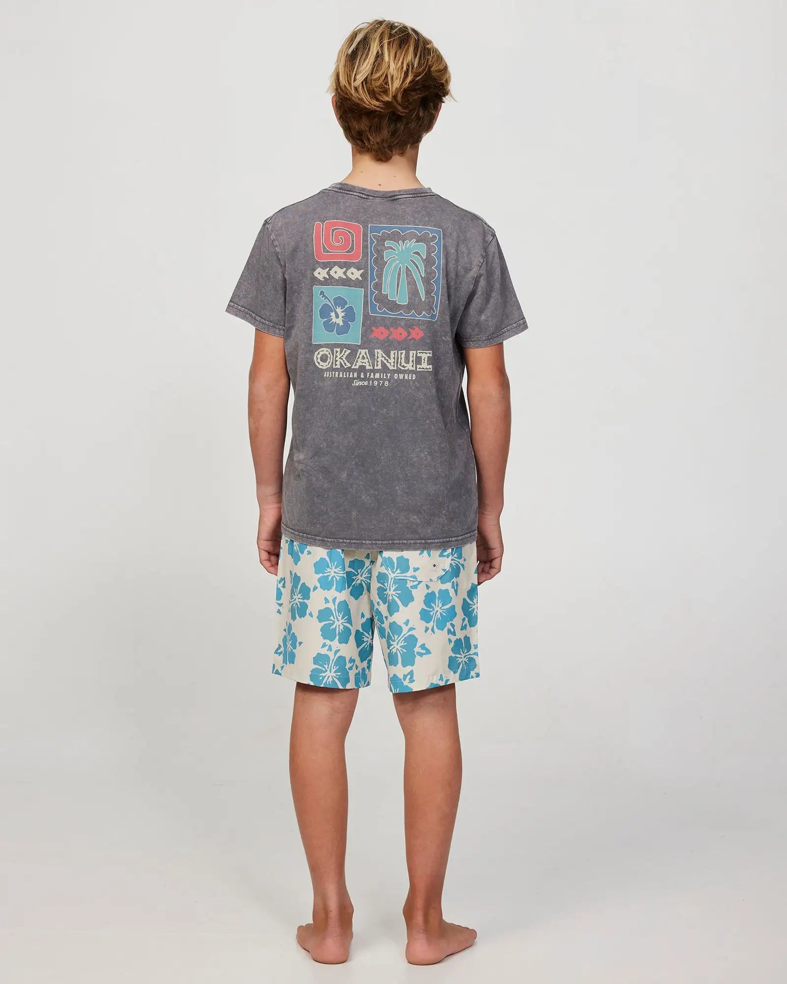 Full body back view of a boy model wearing the Okanui Waterworld Stretch Swim Short for Boys in Stone Aqua