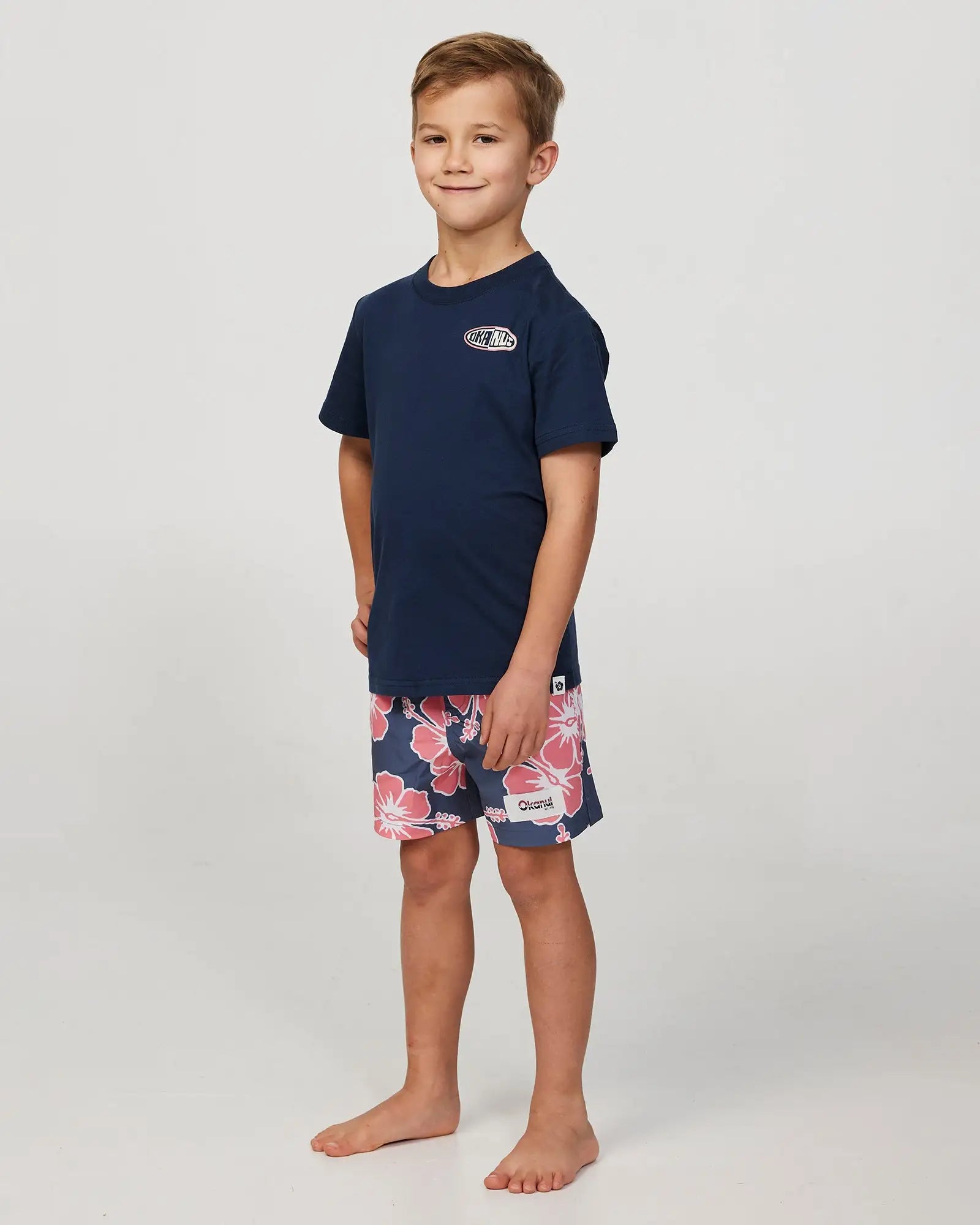 Full body front view of a little boy model wearing the Okanui Way Back When Stretch Swim Short for Boys in Iron Pink