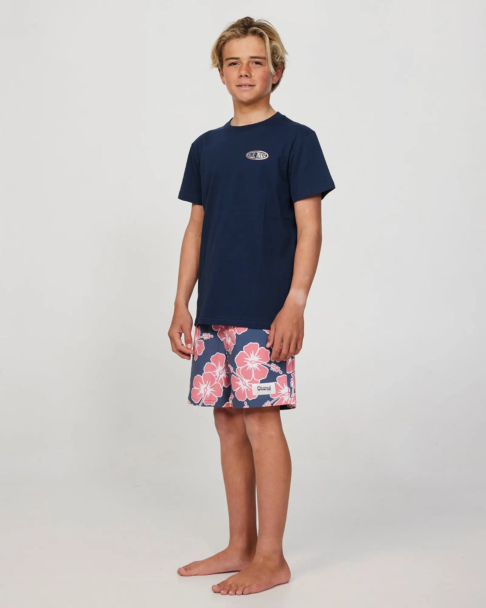 Full body front view of a boy model wearing the Okanui Way Back When Stretch Swim Short for Boys in Iron Pink