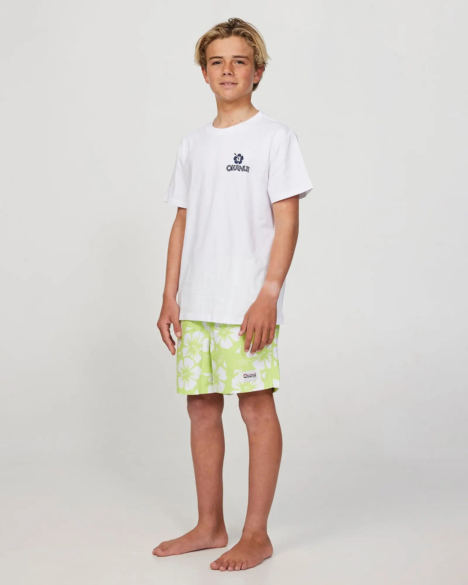 Full body front view of a boy model wearing the Okanui Swim Short for boys in Hibiscus Washed Lime