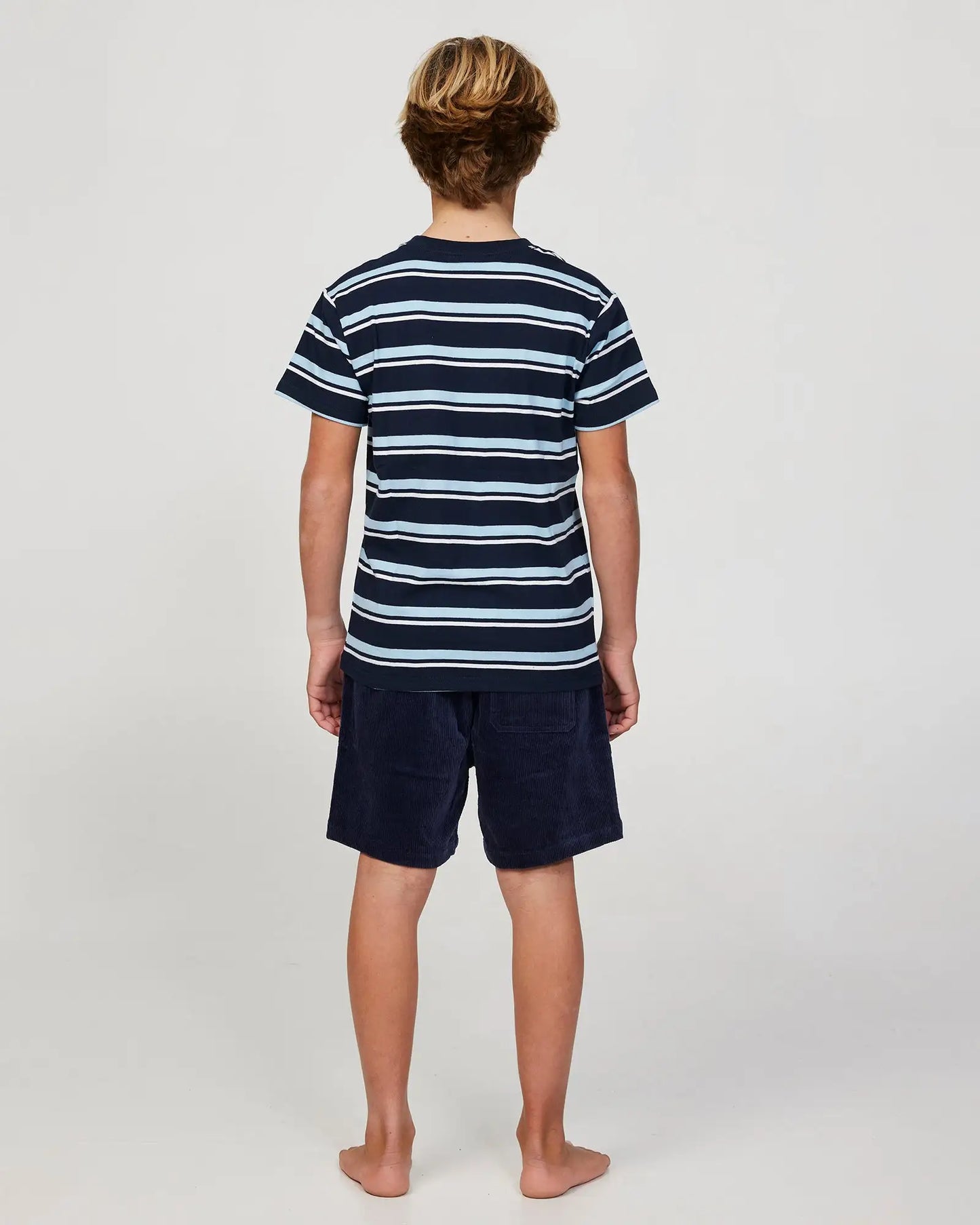 Full body back view of a boy model wearing the Okanui Staple Stripe T-shirt for boys in Navy Multi