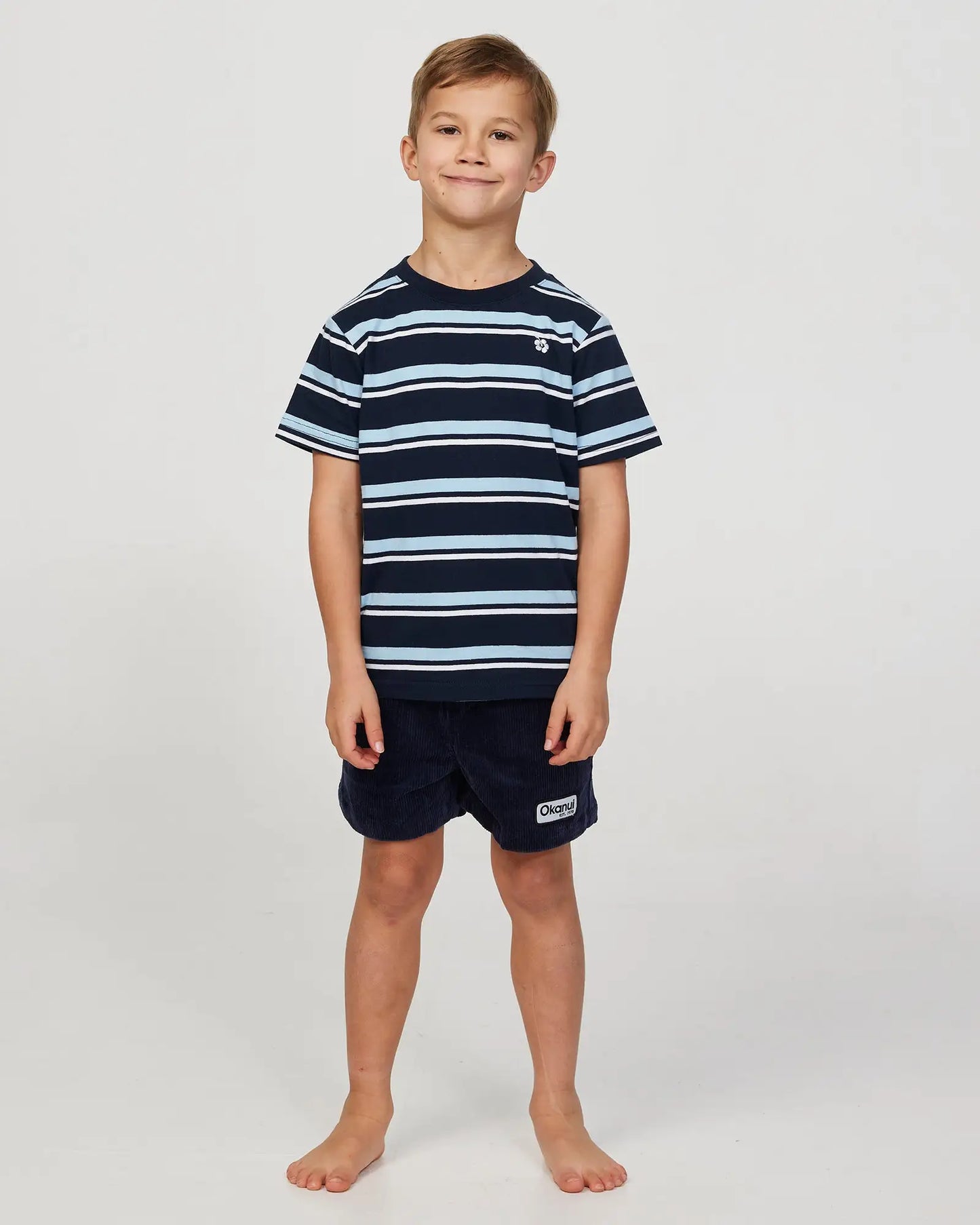 Full body front view of a little boy wearing the Okanui Staple Stripe T-shirt for boys in Navy Multi