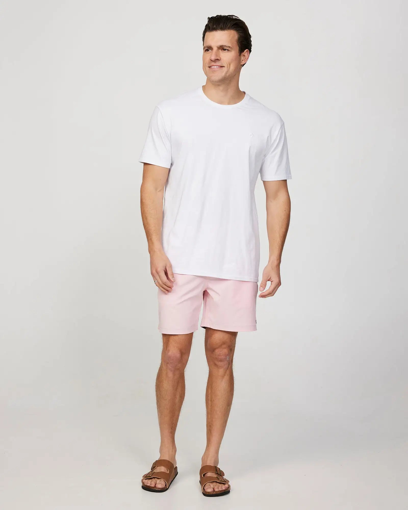 Full body front view of a male model wearing the Okanui Mens Onboard stretch swim short in Pink paired with white shirt