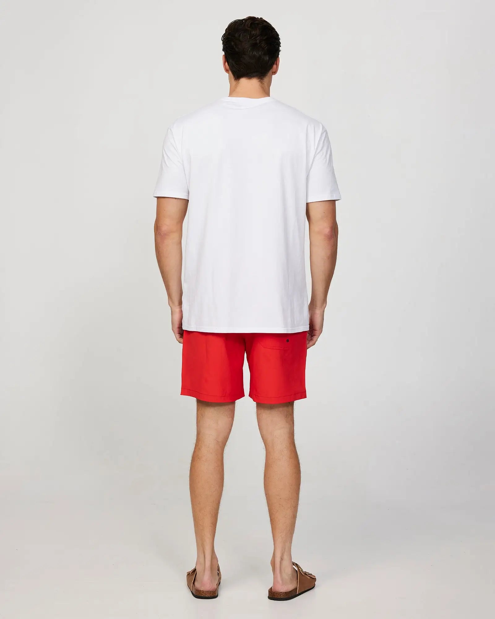 Full body back view of a male model wearing the Okanui Mens Onboard stretch swim short in Red paired with a white shirt