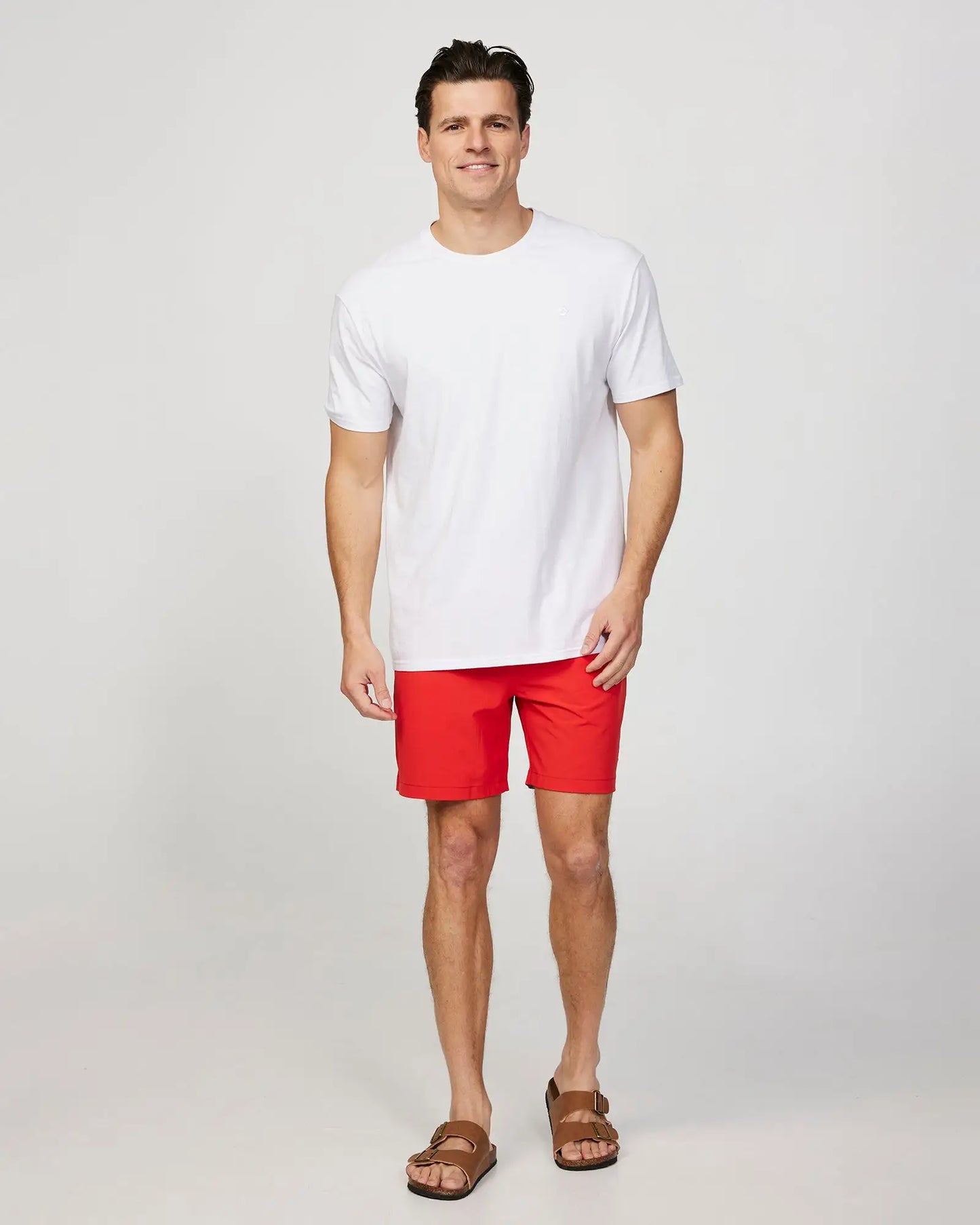 Full body front view of a male model wearing the Okanui Mens Onboard stretch swim short in Red paired wit a white shirt