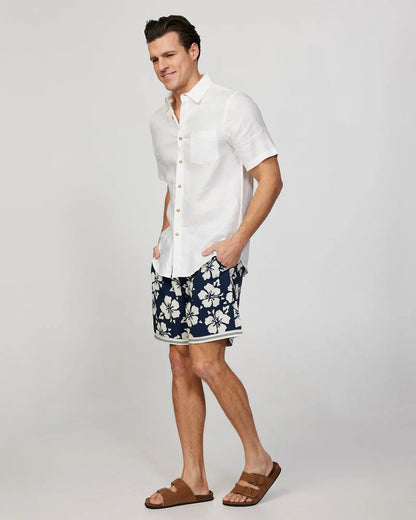 Full body left side view of a male model wearing the Okanui Mens Stonecutter stretch swim short in Navy Natural paired with a white button up shirt