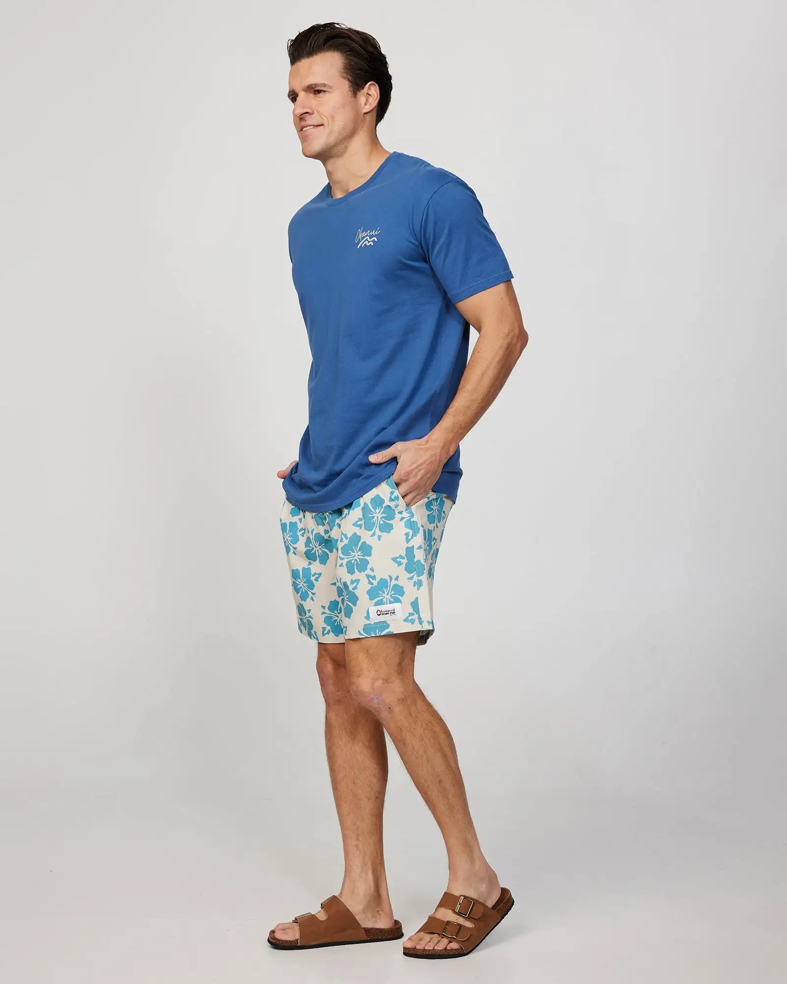 Left side view of a male model wearing the Okanui Mens Waterworld stretch swim short in Stone Aqua paired with a blue T-shirt