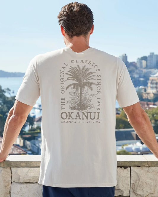 Closeup back view of a male model wearing the Okanui Mens Barrel Tee T-shirt in Stone