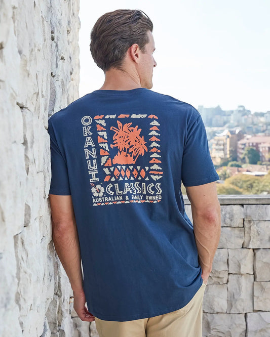 Back view of a male model leaning on the wall wearing the Okanui Mens Breeze Tee T-shirt in Navy