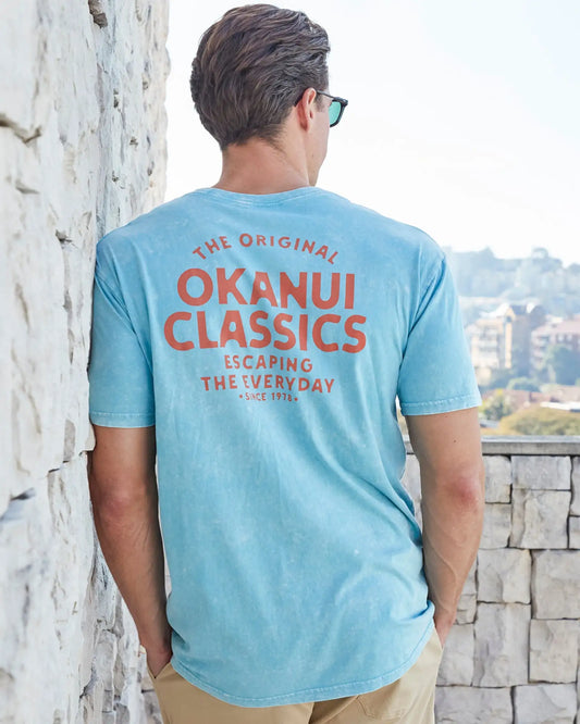 Back view of a male model leaning on a wall wearing the Okanui Mens Decal Tee T-shirt in Seafoam