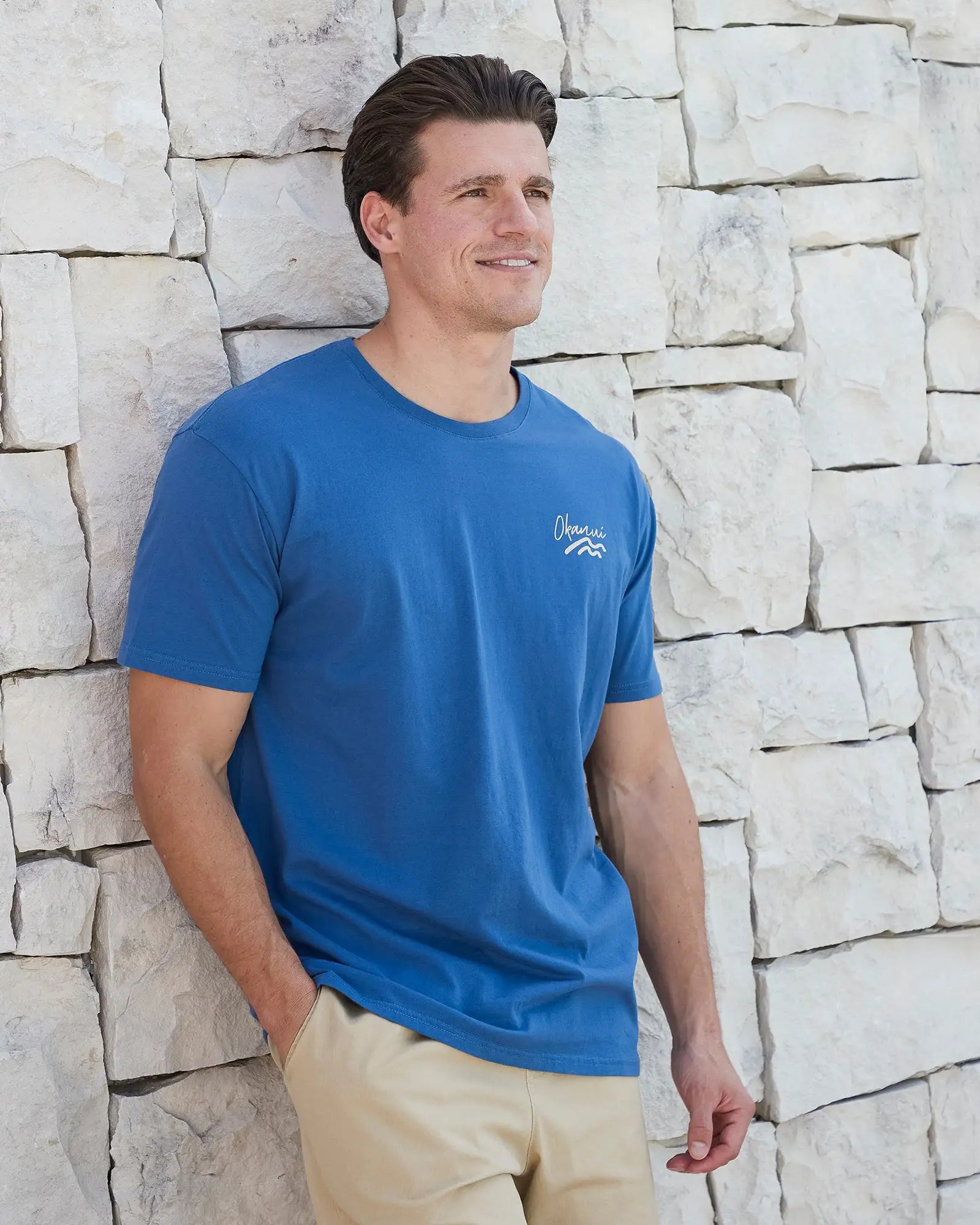 Front view of a male model leaning on a wall wearing the Okanui Mens Ripple Tee T-shirt in Washed Navy