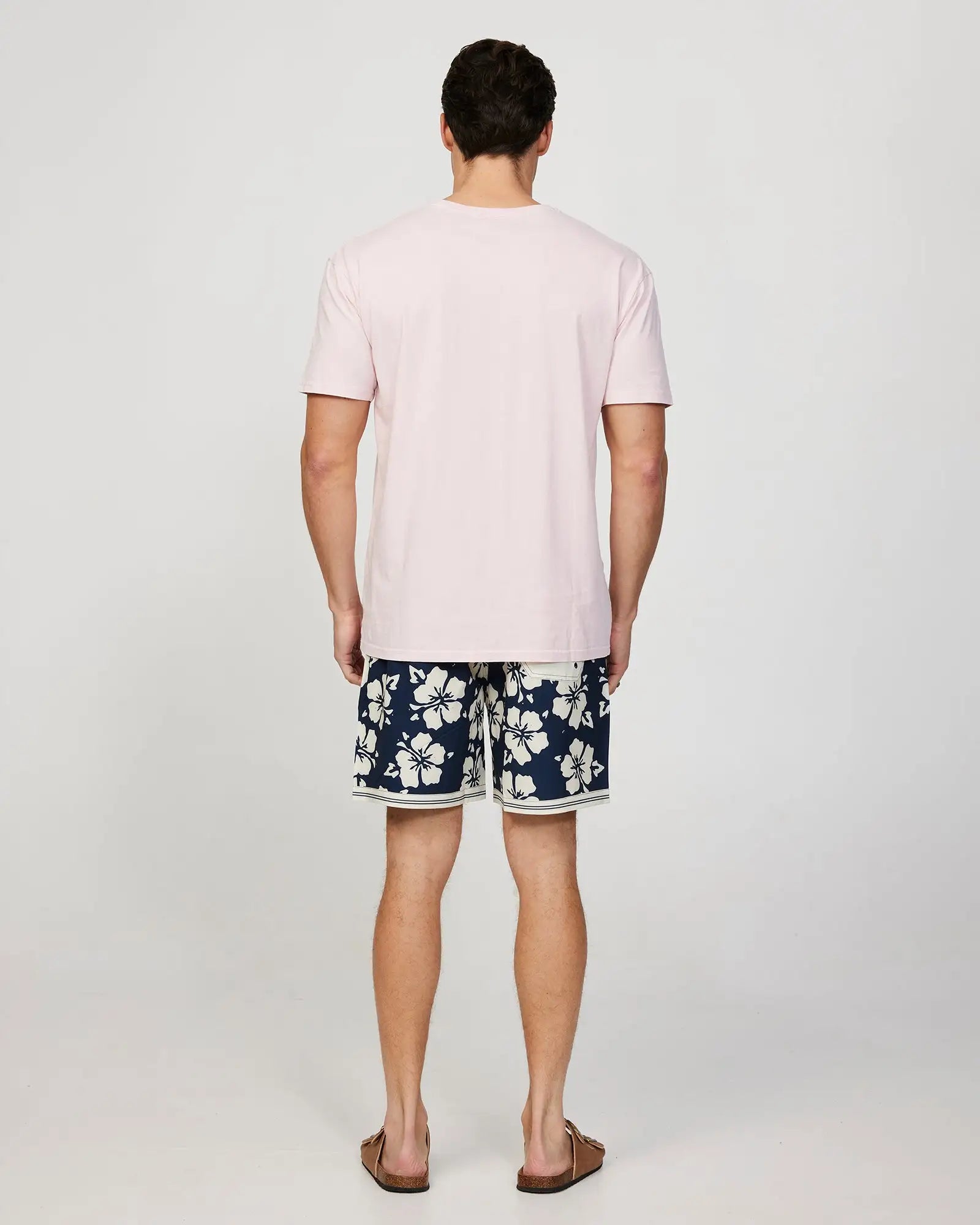 Full body front view of a male model wearing the Okanui Mens Staple Tee T-shirt in pink paired with a hibiscus navy short