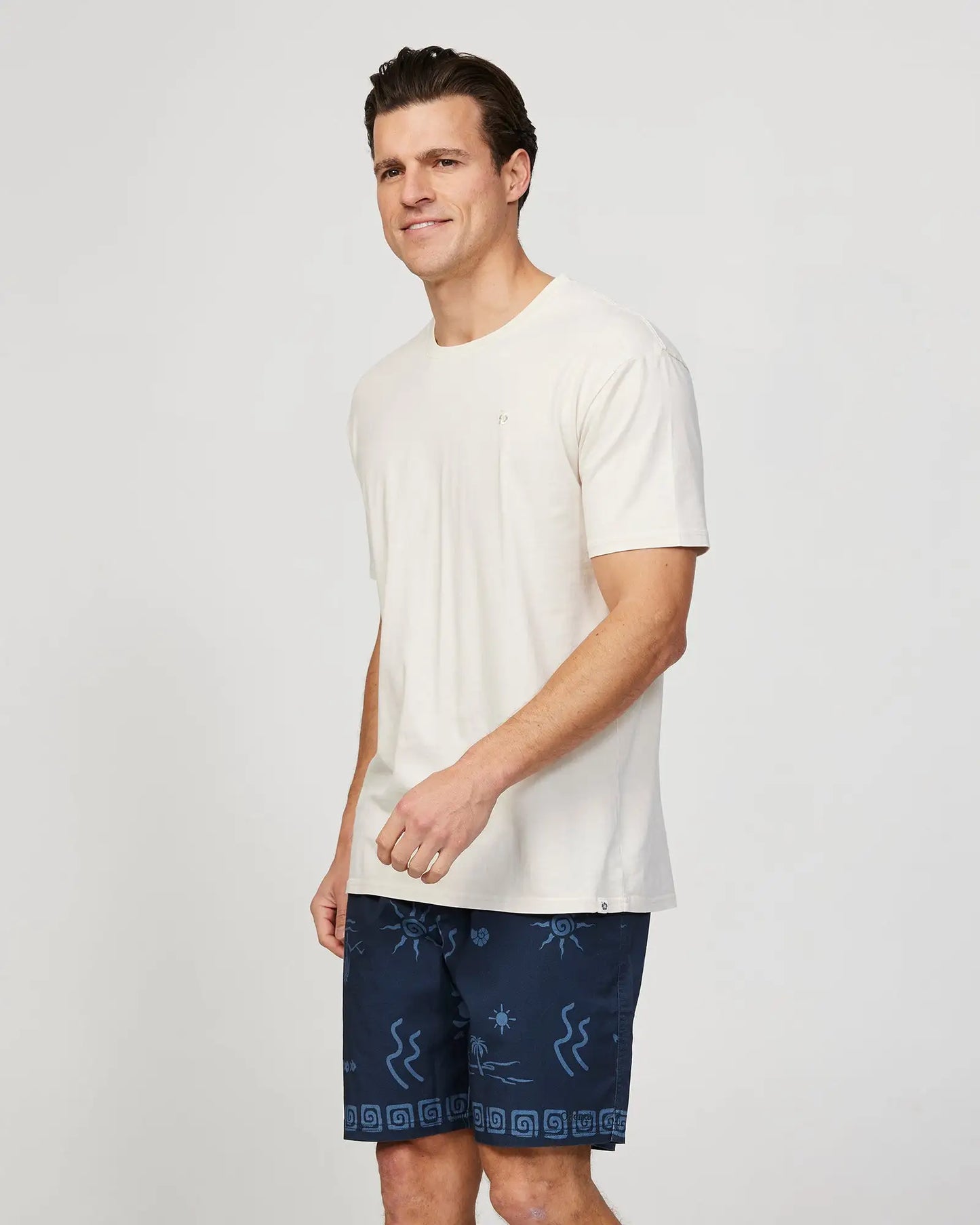 Full body left side view of a male model wearing the Okanui Mens Seascape Walk Short in Navy paired with a white shirt