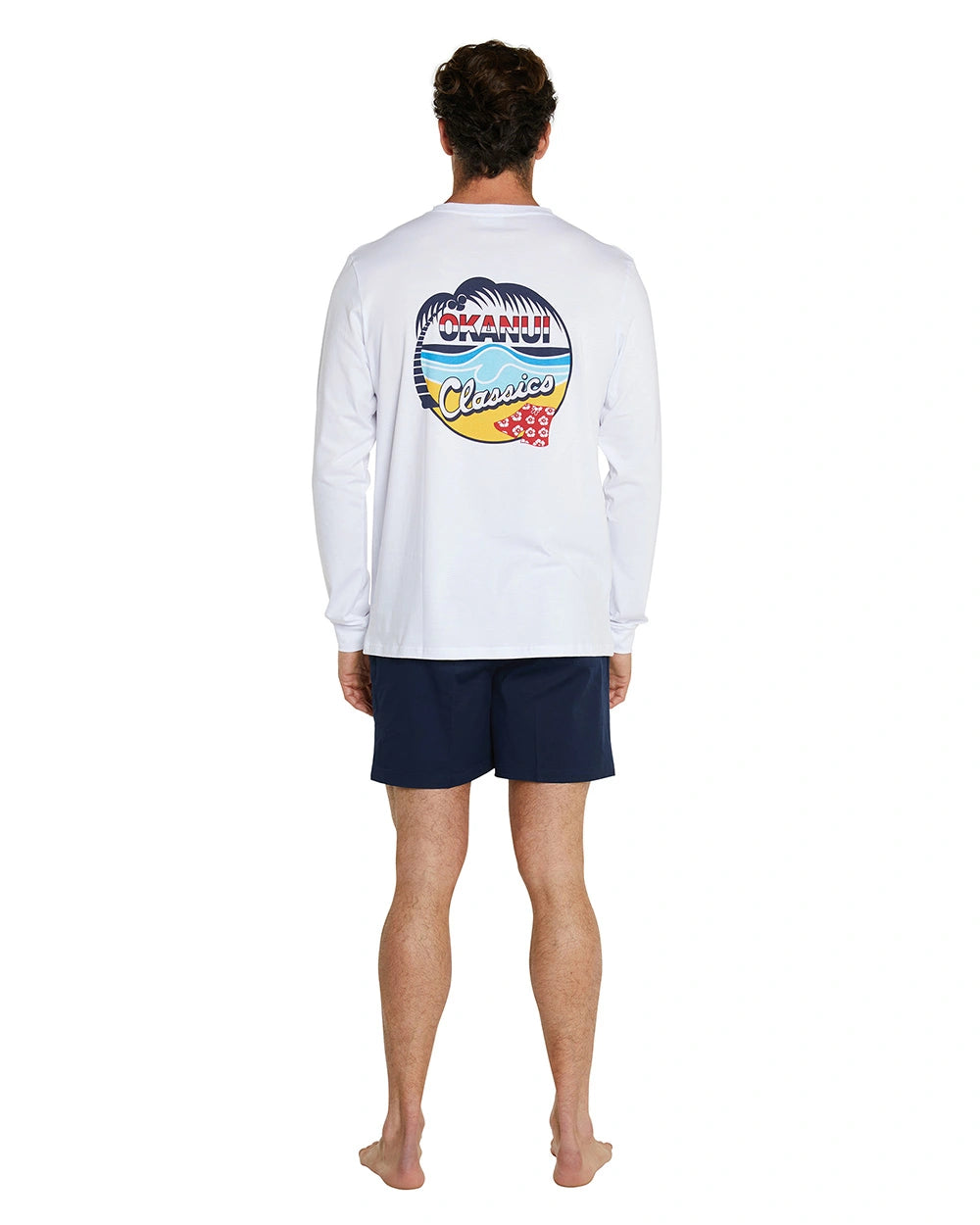 A full view of the Okanui Classic long sleeve t-shirt in white worn by a model wearing blue shorts..