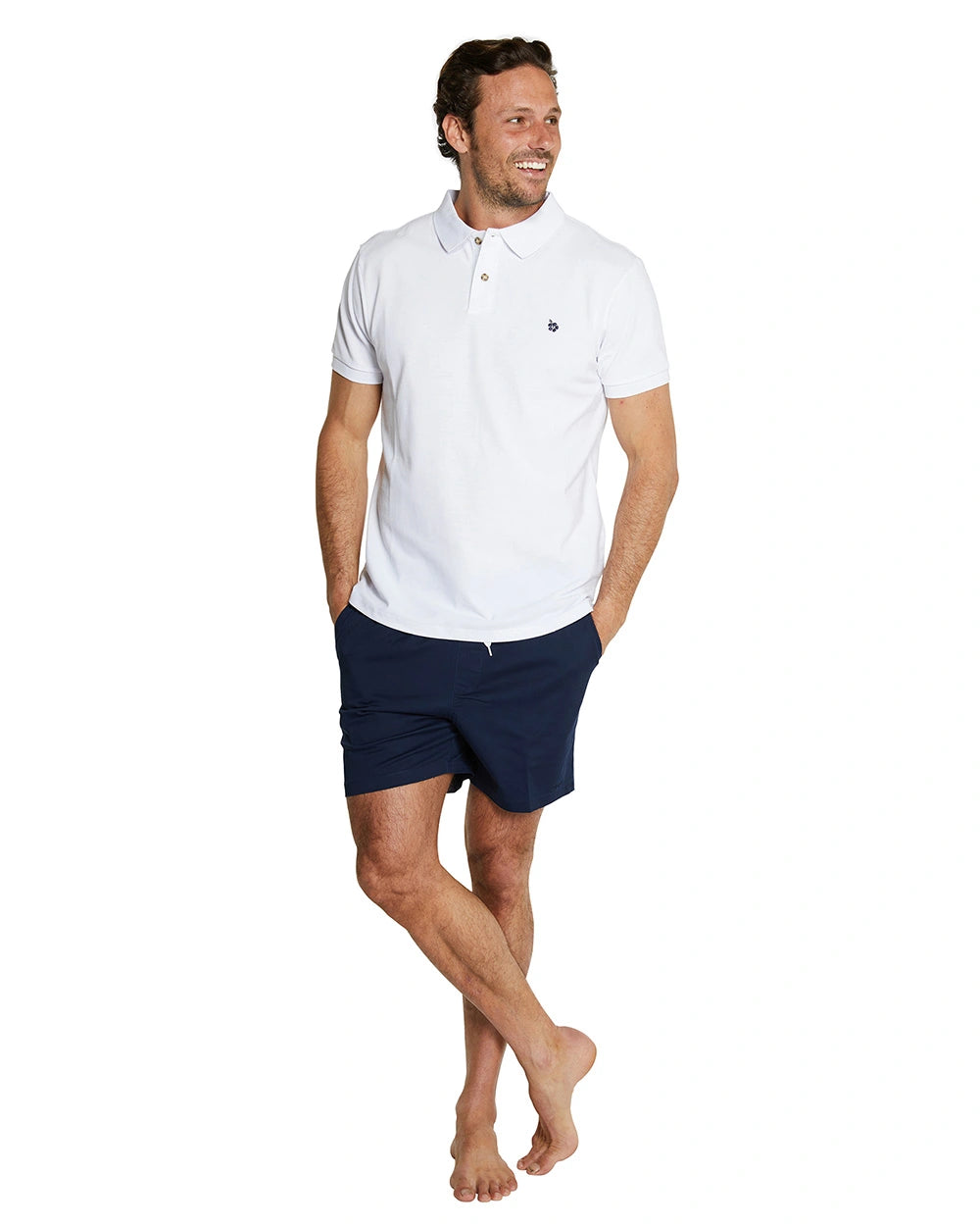 A model smiling and posing wearing the Okanui Classic Polo Shirt in white color paired with navy shorts.