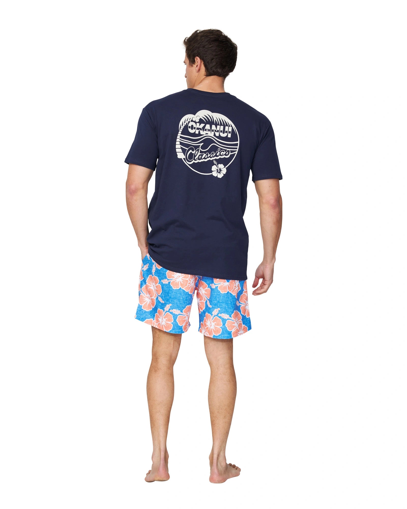 A full body back view of a male model wearing the Okanui Classic Badge Tee in navy color.