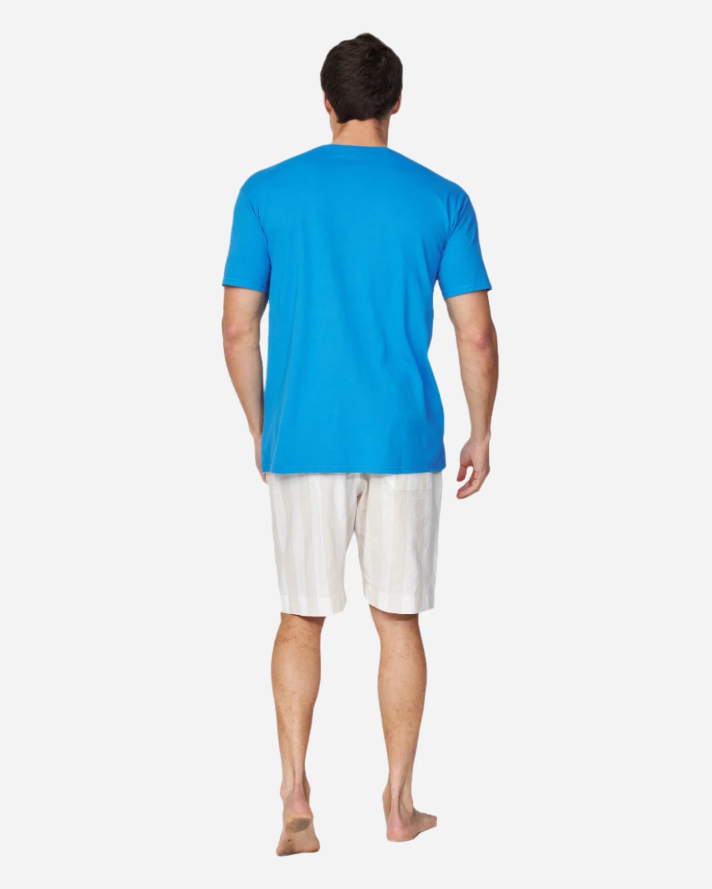 A male model is posing with his back on the camera showcasing the compatibility of the Okanui Staple Tee in washed blue color and a walkshort.