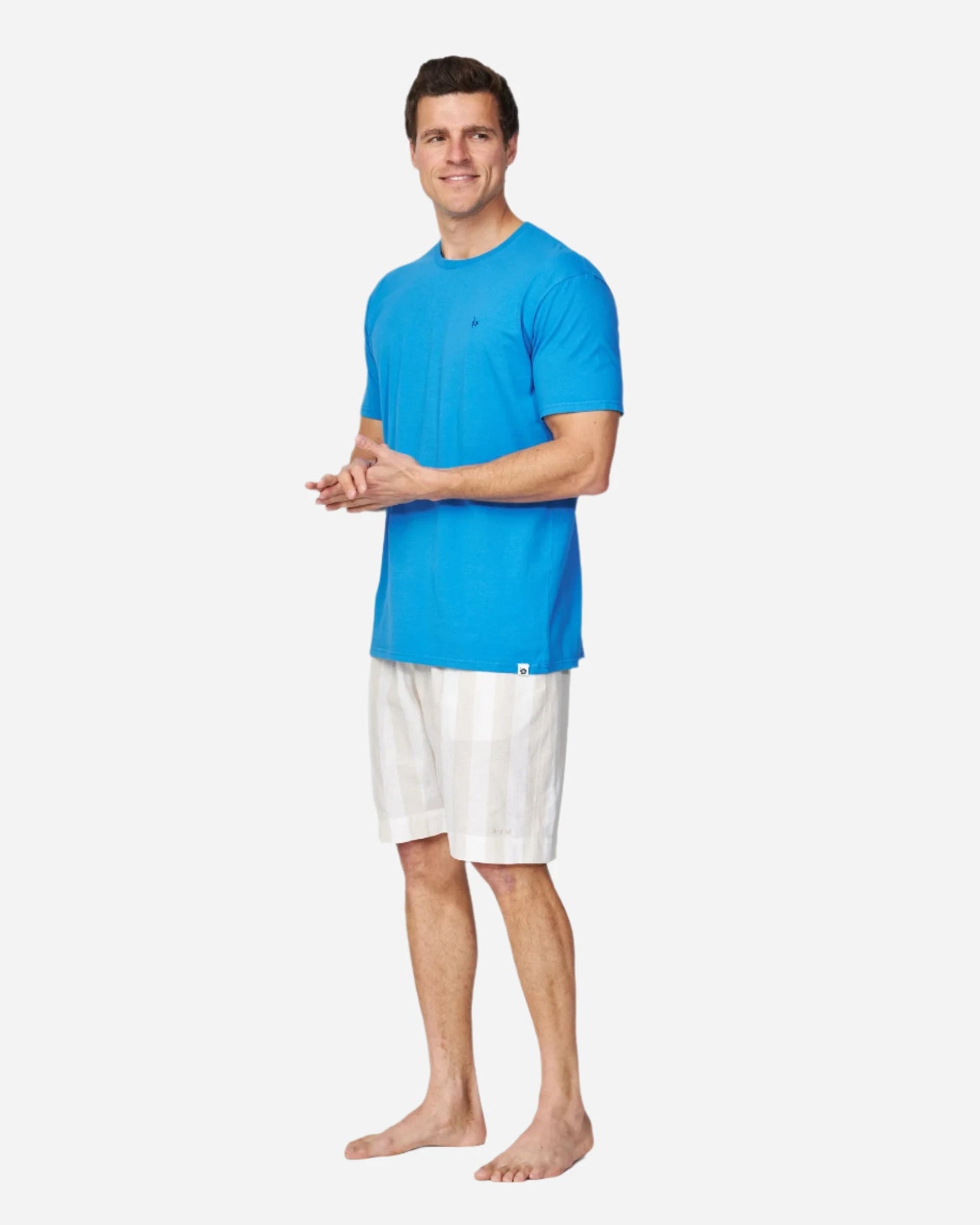 The Okanui Staple Tee worn by a male model in washed blue color is paired with a linen walk shorts.