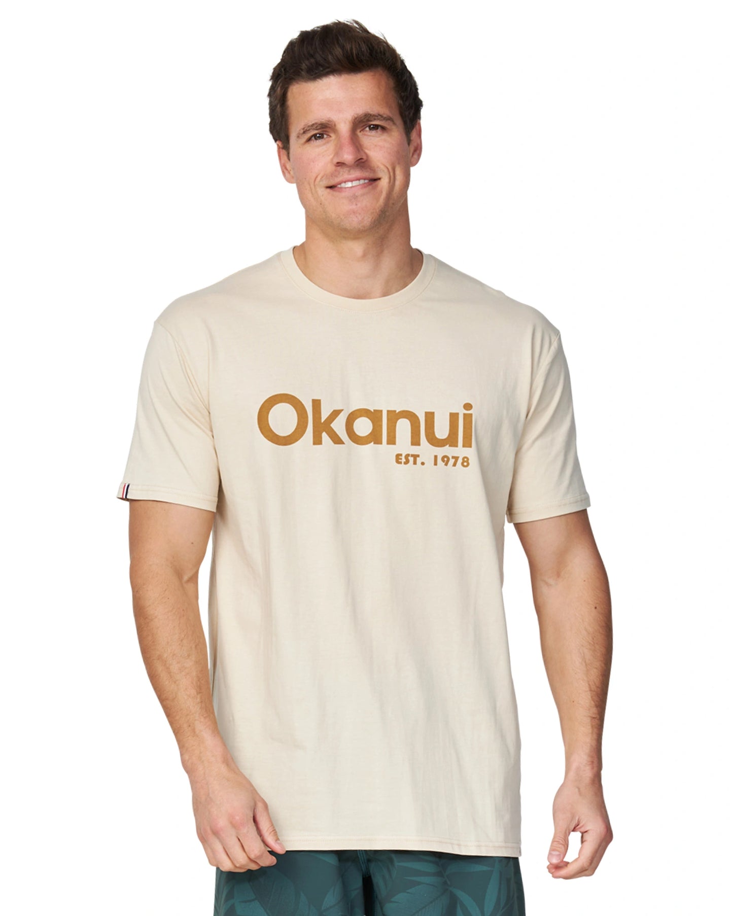 A male model wearing the Okanui Men's Logo Tee in birch color.