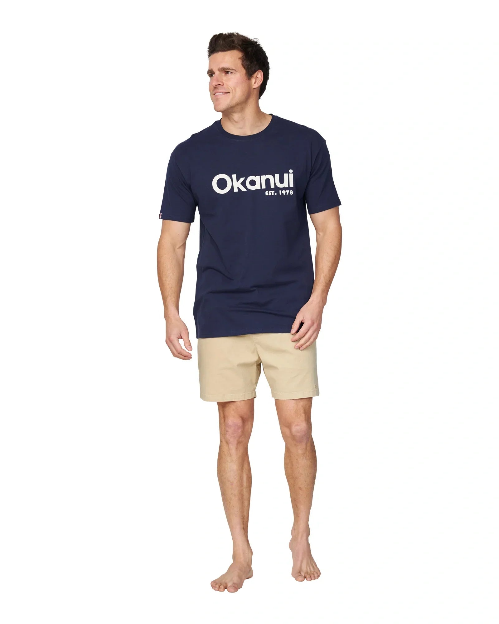 A full body front view of a male model wearing the Okanui Logo Tee in black.