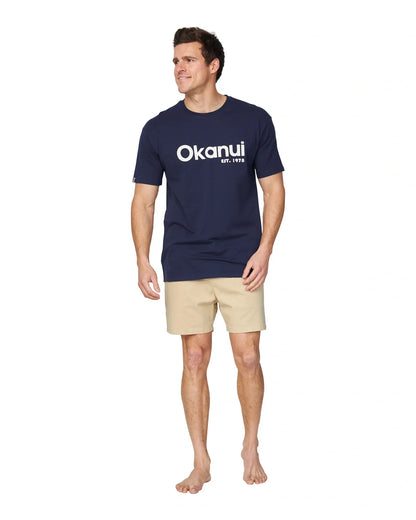 A full body front view of a male model wearing the Okanui Logo Tee in black.