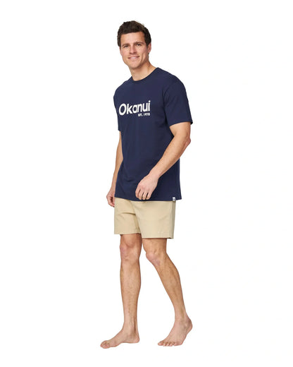 A full body slightly side view of a male model wearing the Okanui Logo Tee in black.