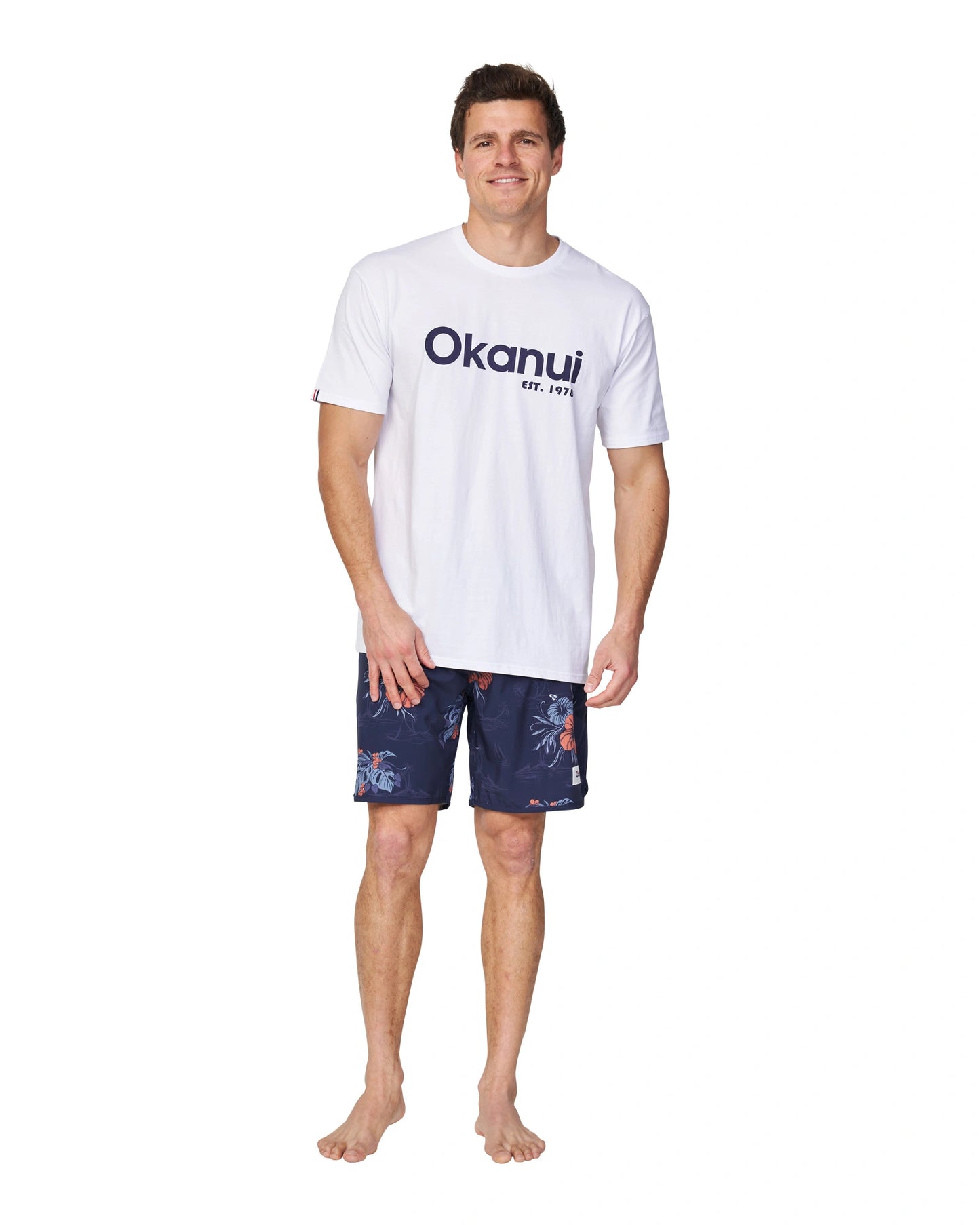 A full body view of a male model wearing the Okanui Logo Tee in white.