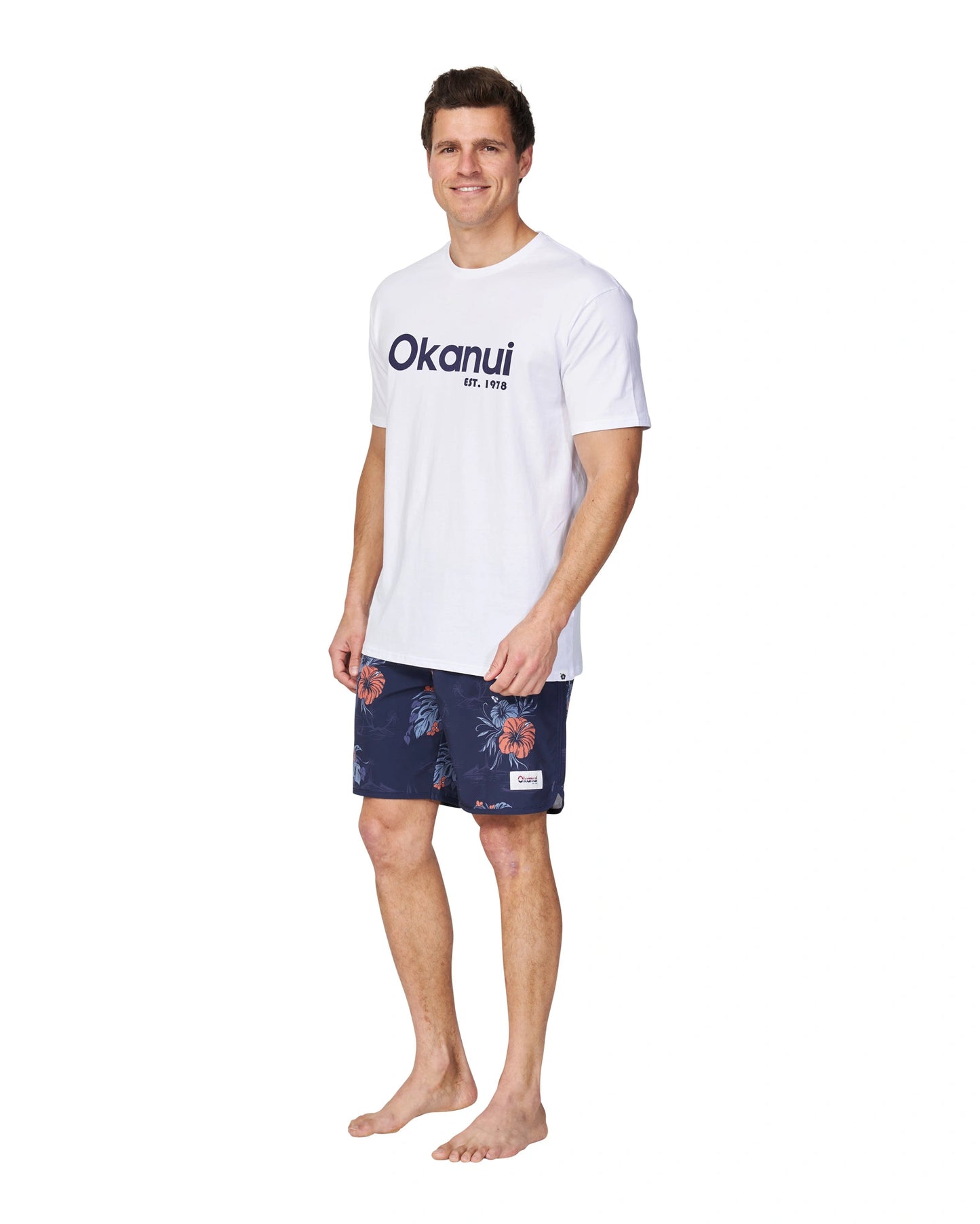 A full body slightly side view of a male model wearing the Okanui Logo Tee in white.