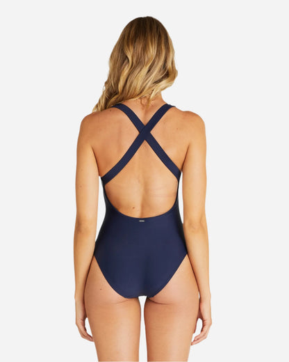 Back view of a female model wearing the  Okanui crossover one piece swimsuit in Navy