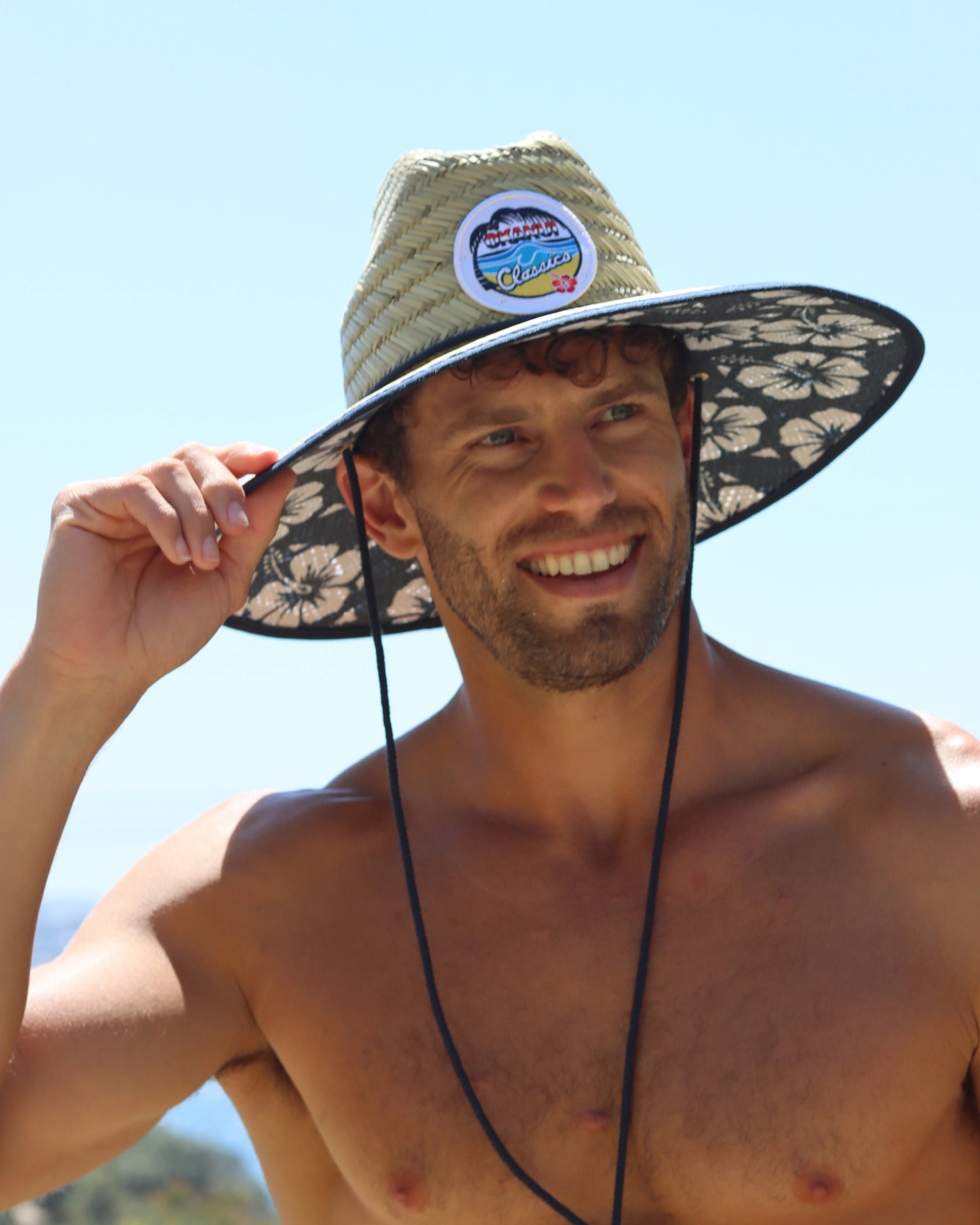 A male model wearing and holding the Okanui wide brim straw hat