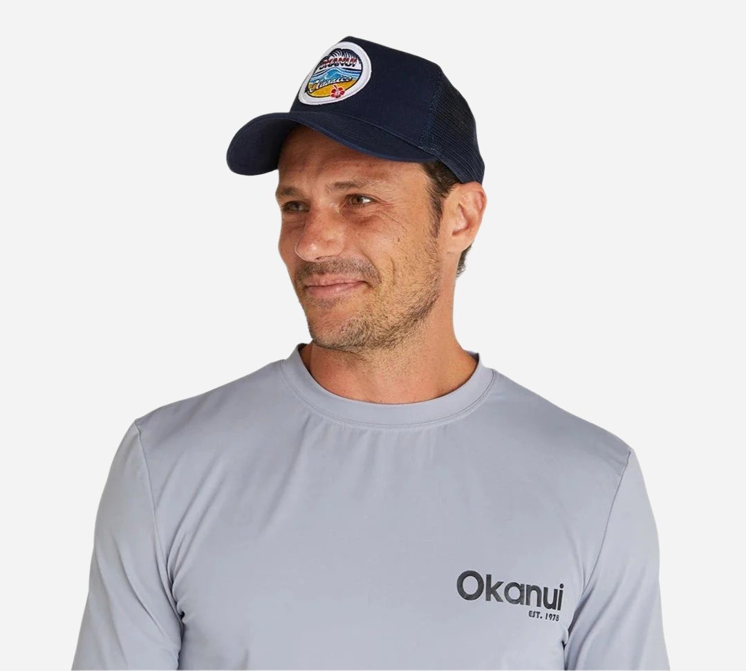 Front view of a male model wearing the Okanui summer access classic badge snapback trucker cap