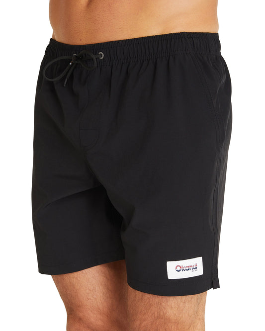 A close-up view of the Okanui Classic Plain Swimshorts for men in black colour featuring its elastic waist and black drawcord and a logo patch on the left leg of the shorts.