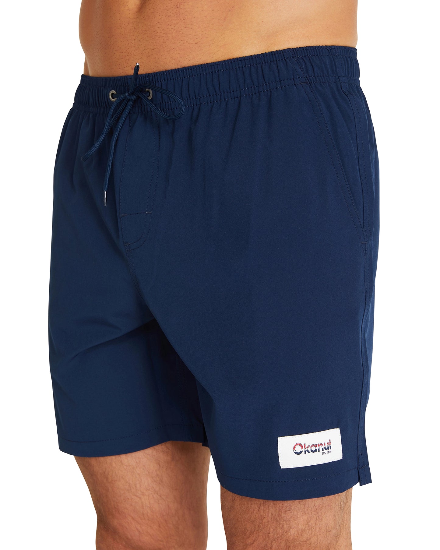 A close-up view of the Okanui Classic Plain Swimshorts for men in navy colour featuring its elastic waist and black drawcord and a logo patch on the left leg of the shorts.