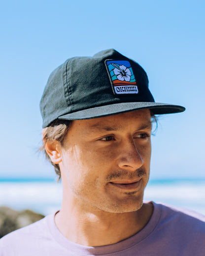 Front view of a male model wearing the Okanui Soundwave Snapback Trucker Cap in Black Color